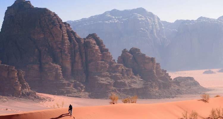 Persoon die op een zandduin staat met rotsachtig bergachtig terrein.