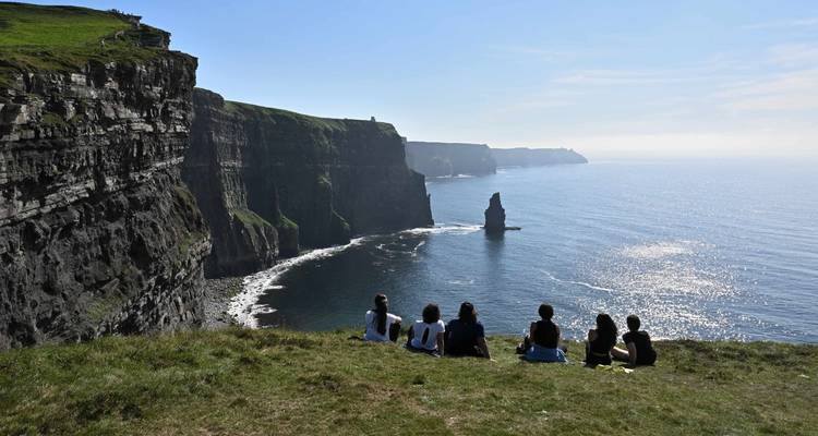 Un groupe de visiteurs assis sur les falaises herbeuses surplombant les spectaculaires falaises de Moher et l'océan Atlantique