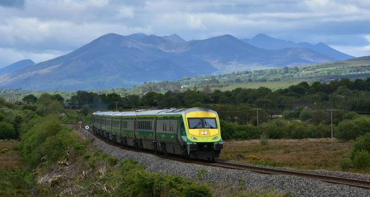 Train vert et jaune d'Irish Rail serpente à travers la campagne avec un arrière-plan montagneux