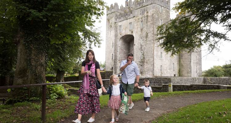 Une famille avec de jeunes enfants passe devant un château de pierre médiéval entouré de verdure