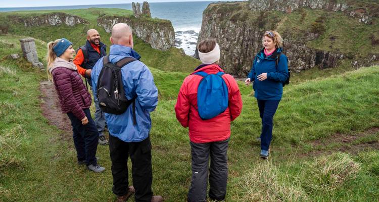 Un guide parle à des randonneurs sur des falaises herbeuses surplombant la mer et des formations rocheuses