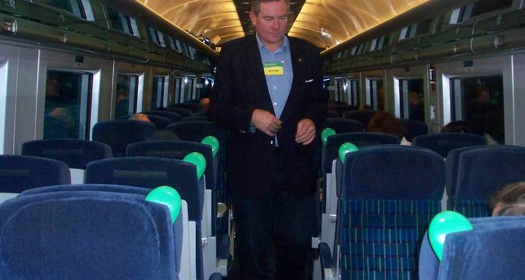 Homme debout dans l'allée d'un wagon de train de voyageurs avec des sièges bleus.