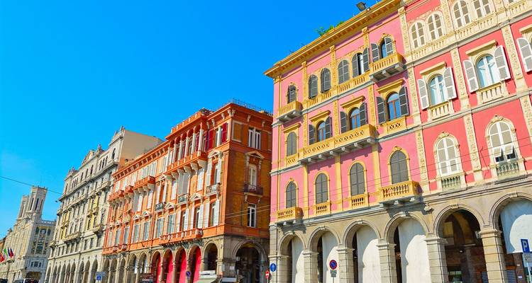 Fila de elegantes edificios históricos con fachadas coloridas y arcos a lo largo de una calle soleada de la ciudad bajo un cielo azul despejado.