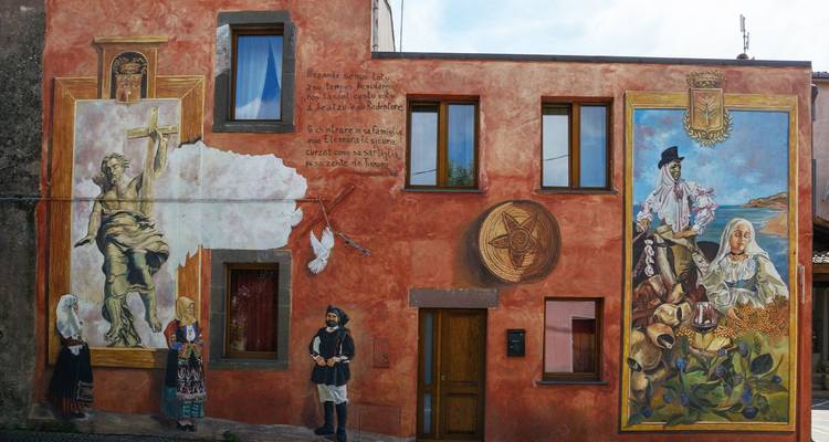 Façade de maison de village richement peinte de fresques murales sardes traditionnelles représentant des gens du cru et le folklore local.