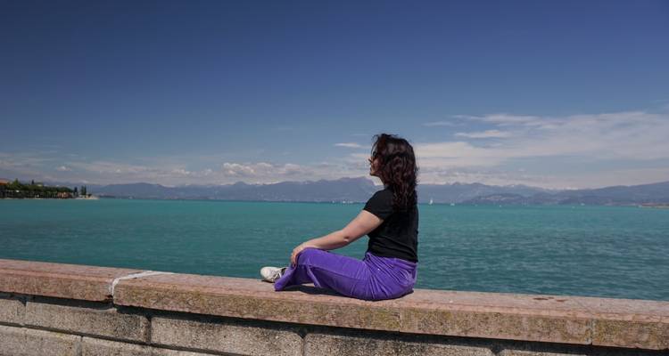 Een persoon die bij een waterlichaam zit met bergen in de verte.