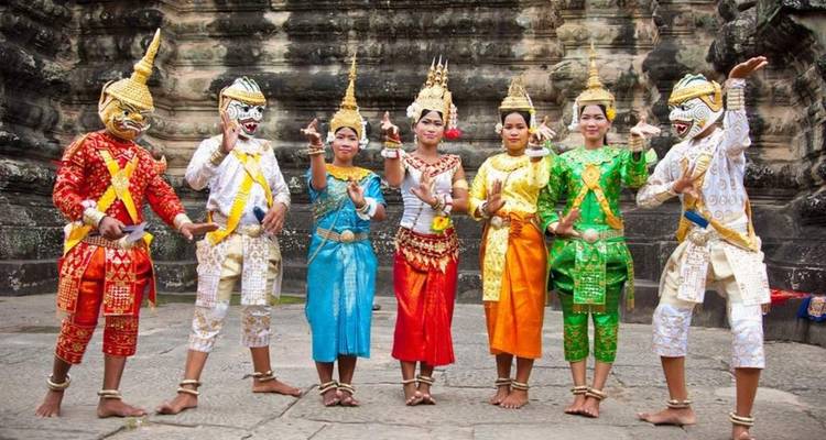 Artistes en costumes traditionnels cambodgiens posant devant un mur de temple ancien.