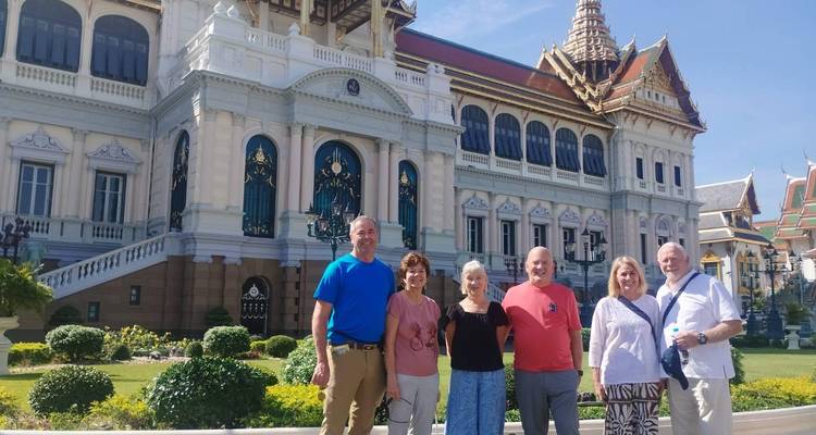 Pequeño grupo de turistas posando frente al ornamentado complejo del Gran Palacio en un día soleado.