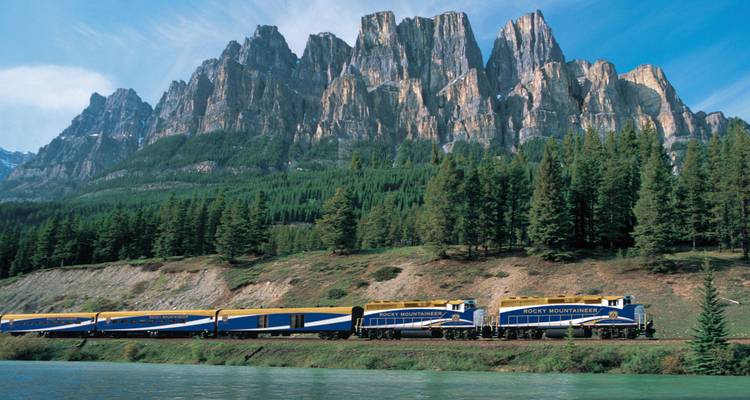 Zug fährt unter markanten zerklüfteten Gipfeln.
