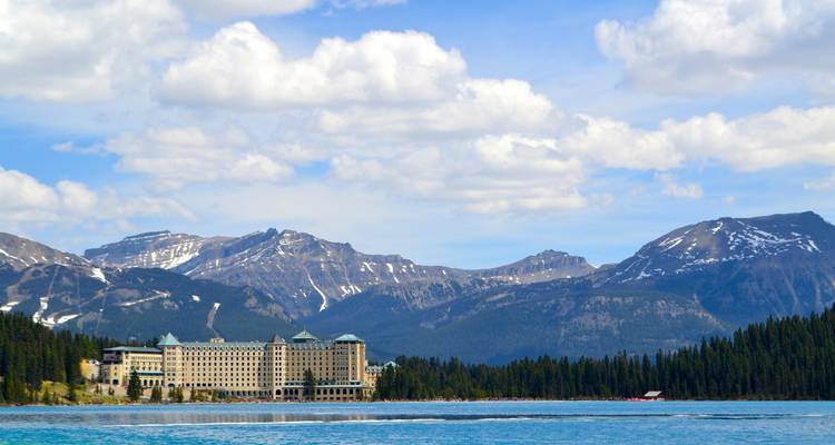 Großes Hotelgebäude an einem See mit Bergblick.