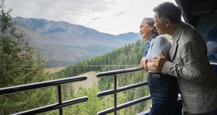 Un couple sourit en profitant de l'air frais de la montagne depuis une plateforme d'observation extérieure du train.