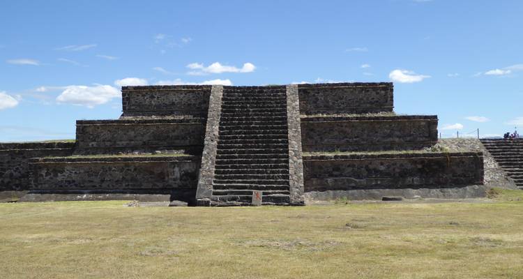A small stone pyramid with stairs in an open field.
