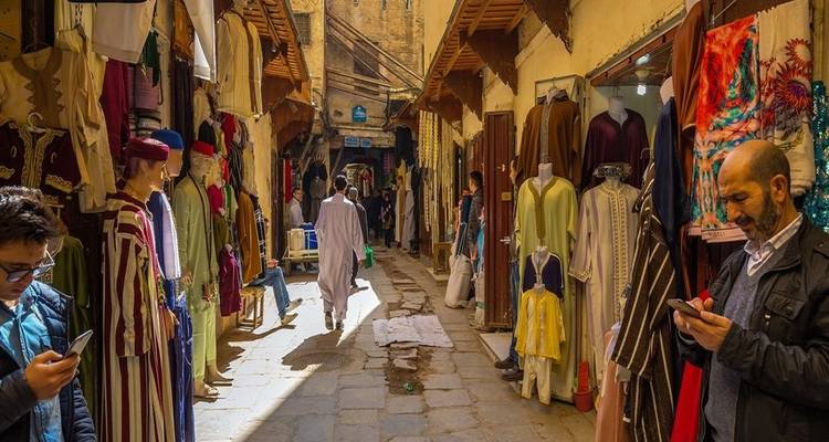 Bustling market street with people shopping, colorful fabrics, and traditional clothing.