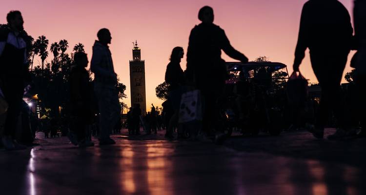 Silhouettes walking in front of the Koutoubia Mosque at dusk.
