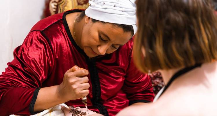 Woman applying traditional henna design on another's hand.