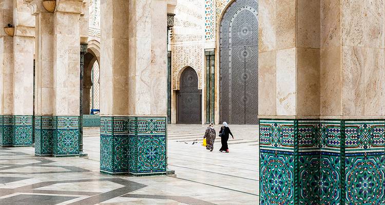 People walking through a grand stone archway with intricate designs.