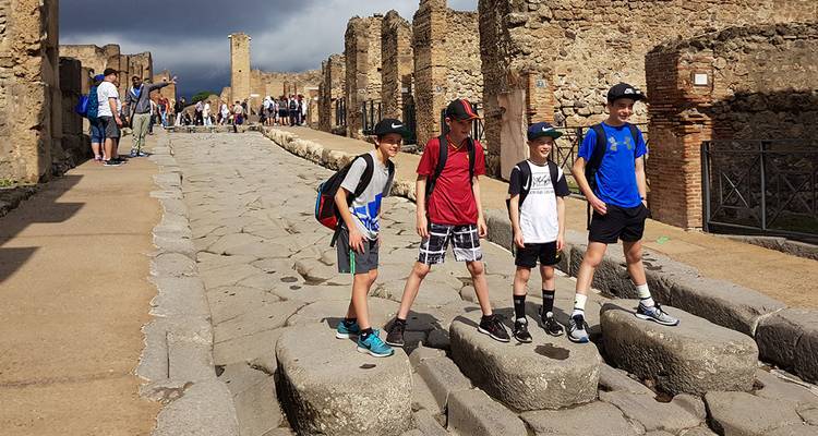 Los niños se paran sobre grandes piedras volcánicas a lo largo de una antigua calle romana en medio de las ruinas de Pompeya.