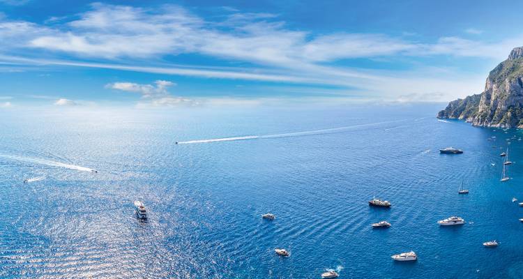 Una vista aérea expansiva de las profundas aguas azules del Mediterráneo salpicadas de yates cerca de los imponentes acantilados de Capri.