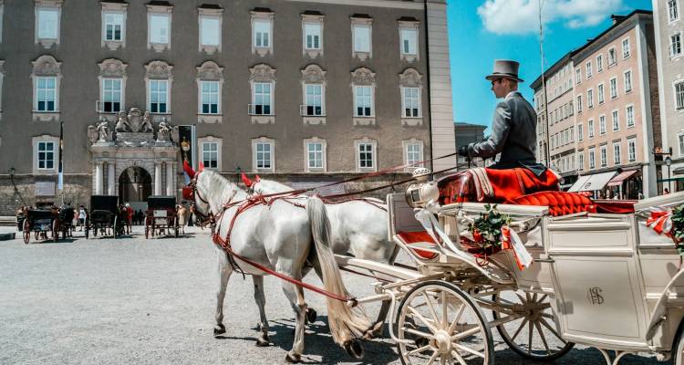 Carrosse tiré par des chevaux avec un cocher portant un haut-de-forme attend sur une place à Salzbourg