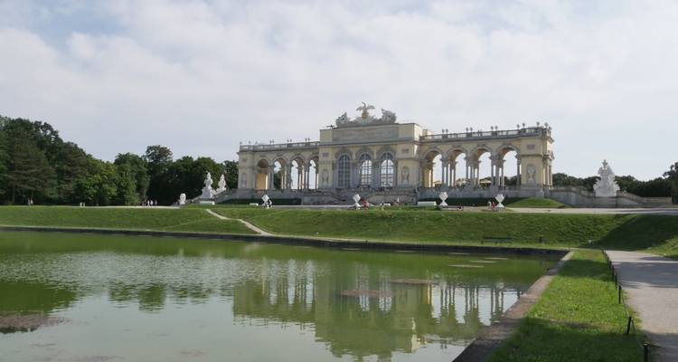 People sitting by a pond in front of a historical colonnaded building.
