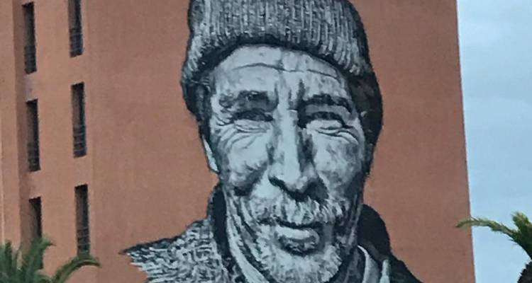 Grote muurschildering van het gezicht van een bejaarde man op een gebouwmuur.