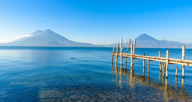 La jetée en bois s'avance dans les eaux bleu cristal du Lac Atitlán avec deux pics volcaniques s'élevant au-delà.