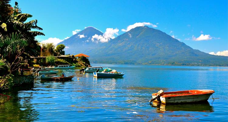 Der ruhige Lago Atitlán mit vertäuten Booten und zwei Vulkangipfeln unter klarem Himmel