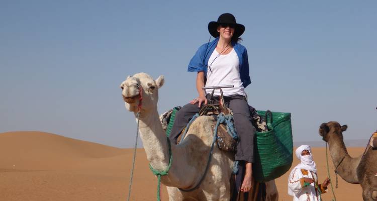 Person riding a camel in a desert with others nearby.