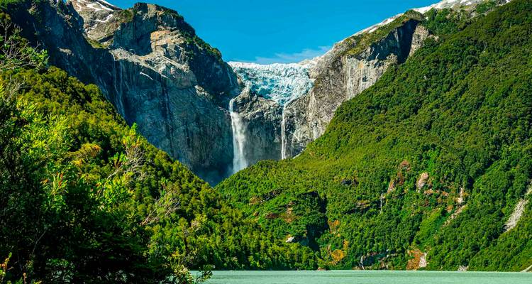 Laguna turquesa bajo un valle exuberante con un glaciar colgante espectacular y una cascada.