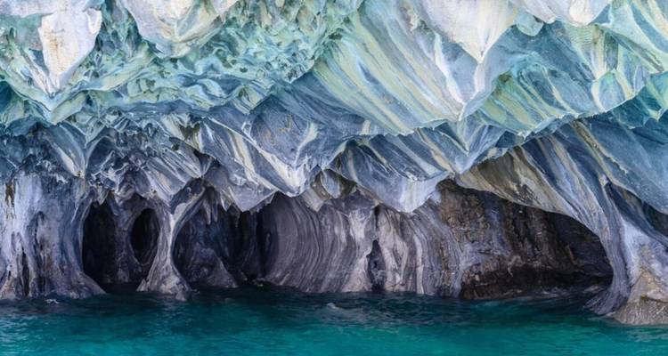 El agua azul verdosa lame las impresionantes cuevas de mármol con formaciones de roca rayada y remolinos.
