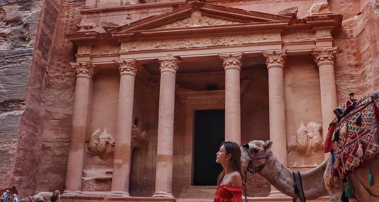 Frau und Kamel vor einer antiken Felsenarchitektur.