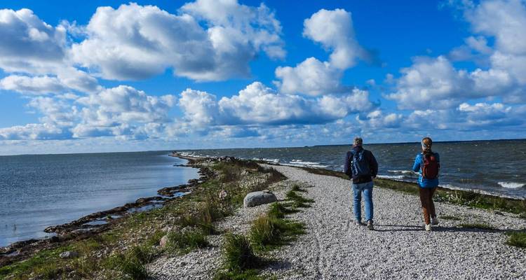 Twee wandelaars die langs een smalle stenen landtong lopen die ver in de Baltische Zee uitsteekt onder een dramatische wolkenlucht.