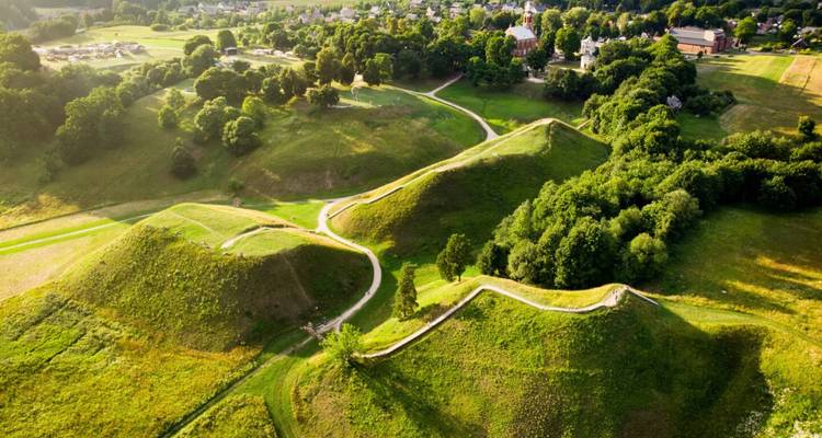 Luchtfoto van glooiende groene vestingswallen verbonden door kronkelende paden en omgeven door bos en dorpje.