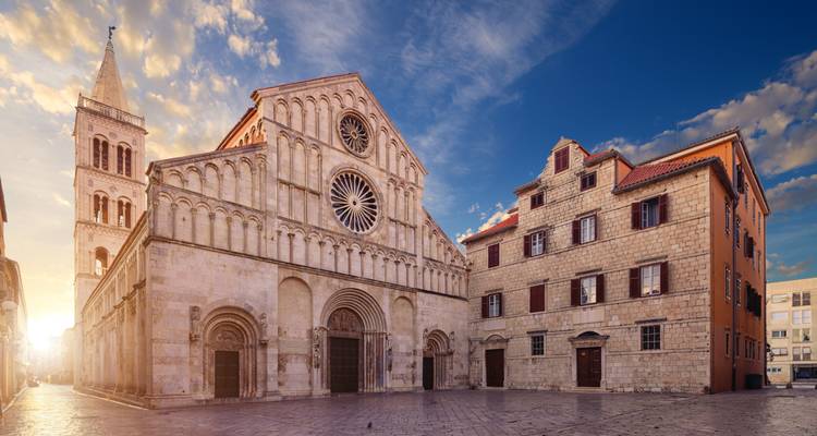 Historic stone building with a tower in a city square at sunset.