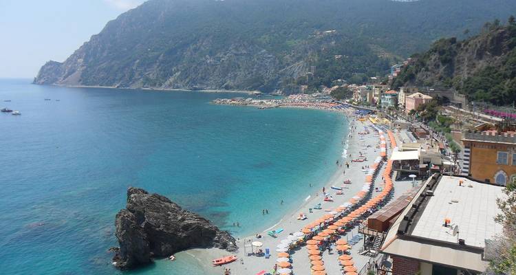 Vue panoramique de la plage de Monterosso al Mare bordée de parasols orange et de la mer Ligure turquoise.