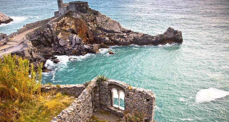 Une forteresse de pierre en ruines se dresse sur un promontoire escarpé surplombant des eaux turquoise et des vagues déferlantes.