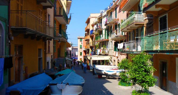 Ruelle ensoleillée dans un village des Cinque Terre bordée de maisons colorées et de bateaux de pêche amarrés.
