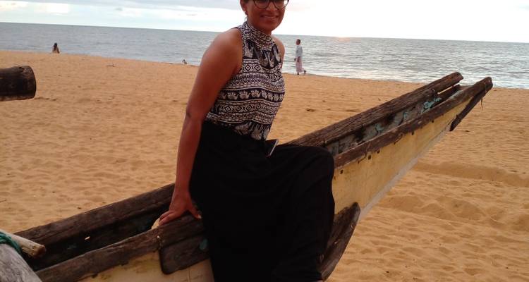 Person sitting on a boat on a beach with the sea in the background.
