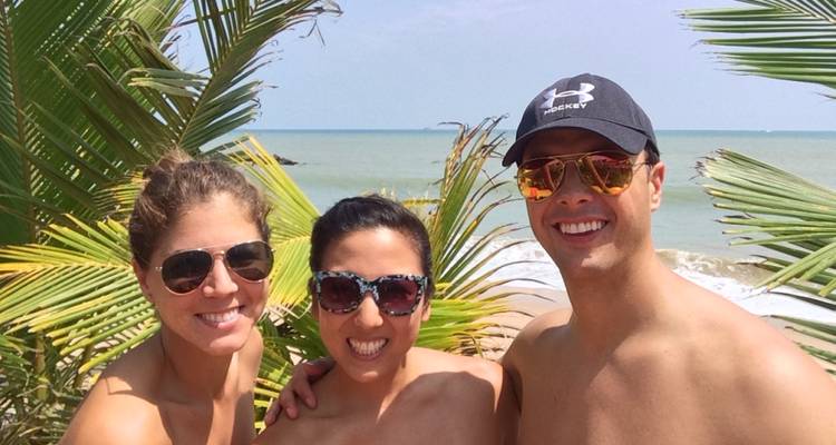 Trois personnes souriantes avec des lunettes de soleil sur une plage.