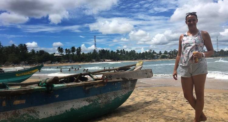 Une femme debout sur la plage à côté d'un bateau traditionnel.
