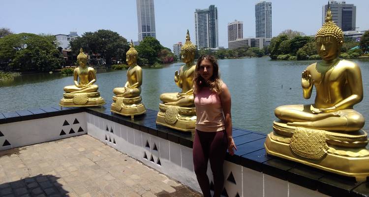 Une femme posant avec des statues dorées de Bouddha près d'un lac avec un horizon urbain.