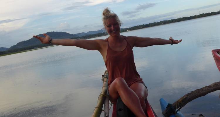 Une femme aux bras étendus assise sur un bateau sur un lac calme.