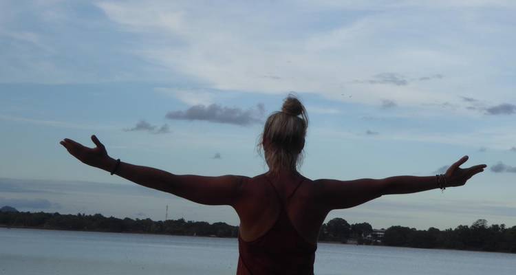 Une femme aux bras étendus face à un lac.