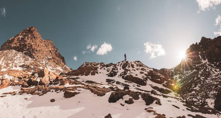 Person, die auf einem schneebedeckten Berggipfel steht, während die Sonne scheint.