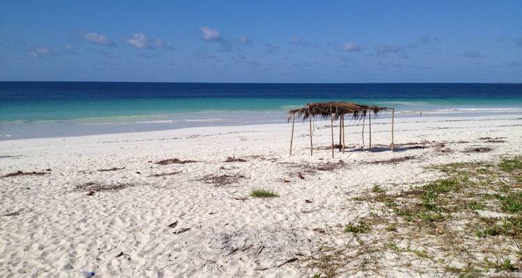 A beach with white sand, blue ocean, and a simple wooden structure.
