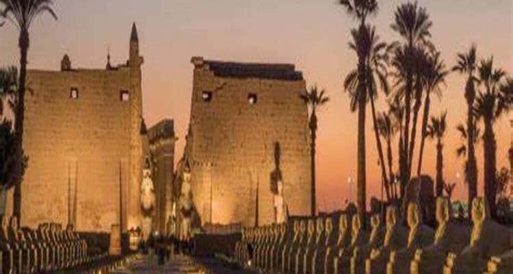 Des pylônes en grès illuminés et des rangées de statues de sphinx menant à un ancien temple égyptien au crépuscule