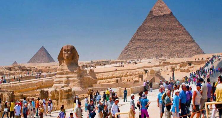 Des foules de touristes explorent le plateau de Giza avec le Grand Sphinx et les pyramides emblématiques sous un ciel dégagé