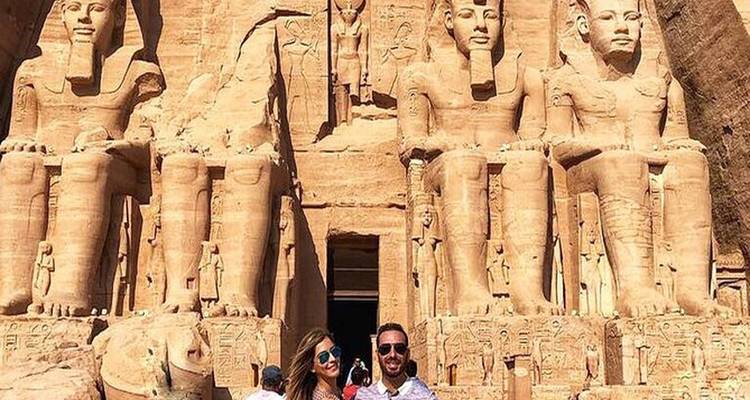 Couple rayonnant devant les statues colossales taillées dans la roche d'Abu Simbel sous un ciel dégagé.