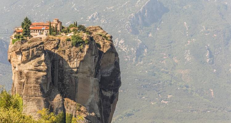 Monasterio en un acantilado rocoso empinado con vistas a un valle exuberante.