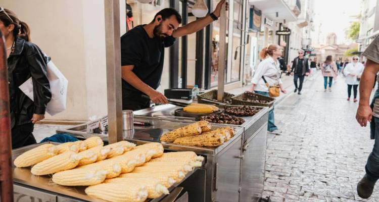 Vendedor ambulante vendiendo maíz y castañas en una calle concurrida.