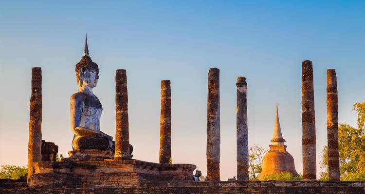 Silueta de estatua de Buda y estupa antigua al atardecer.